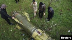 Сирийские повстанцы в провинции Дераа разглядывают обломок ракеты
