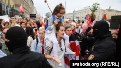A woman carrying a girl confronts riot police during a women's march in Minsk against election fraud and police violence on August 29, 2020. 