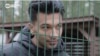 Iranian migrant Amir Chani speaks with Current Time through the fence surrounding Latvia's Mucenieki detention center for illegal migrants. A recent outbreak of COVID-19 cases led to all of the center's 262 residents being placed under quarantine. 